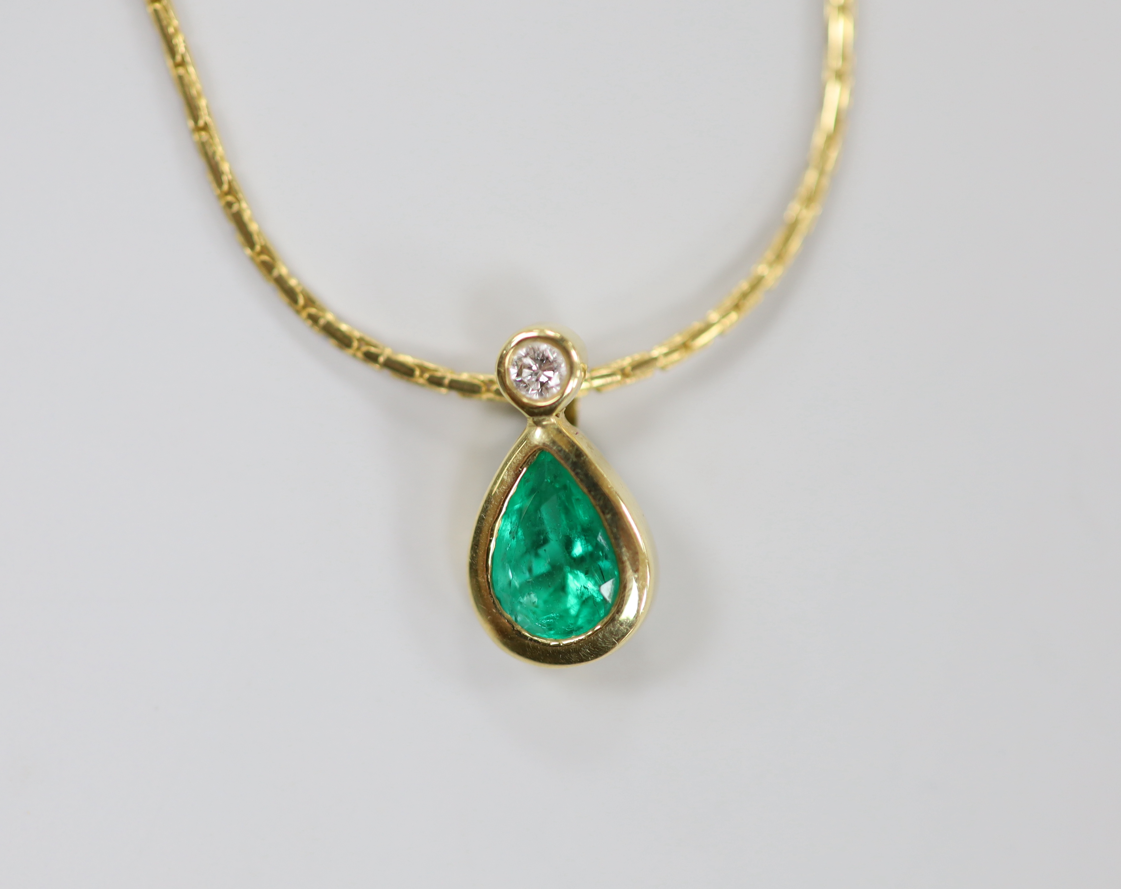 A modern 18ct gold, pear cut emerald and round cut diamond set pendant, 14mm, on an 18ct gold chain, 38cm, gross weight 6.3 grams.